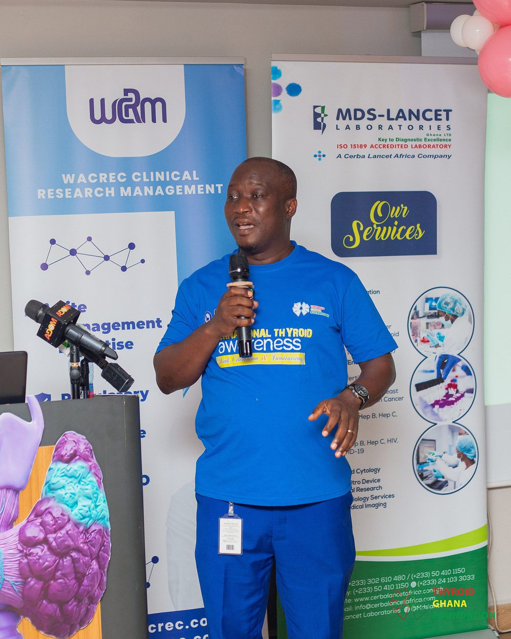 A presenter explaining treatment options for thyroid disorders beside the event banners.